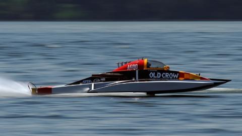 Black and red hydroplane race boat labeled “Old Crow” speeding across calm water during an APBA boat race.