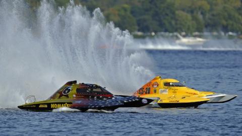 Two inboard hydroplane race boats compete side by side on the water, with large spray plumes rising behind them during a boat race.